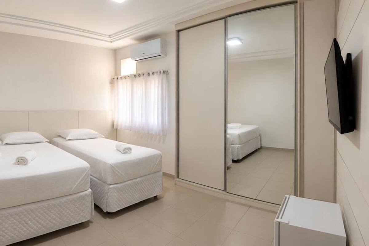 A hotel room with two beds, a wardrobe, a television, and an air conditioning unit.
