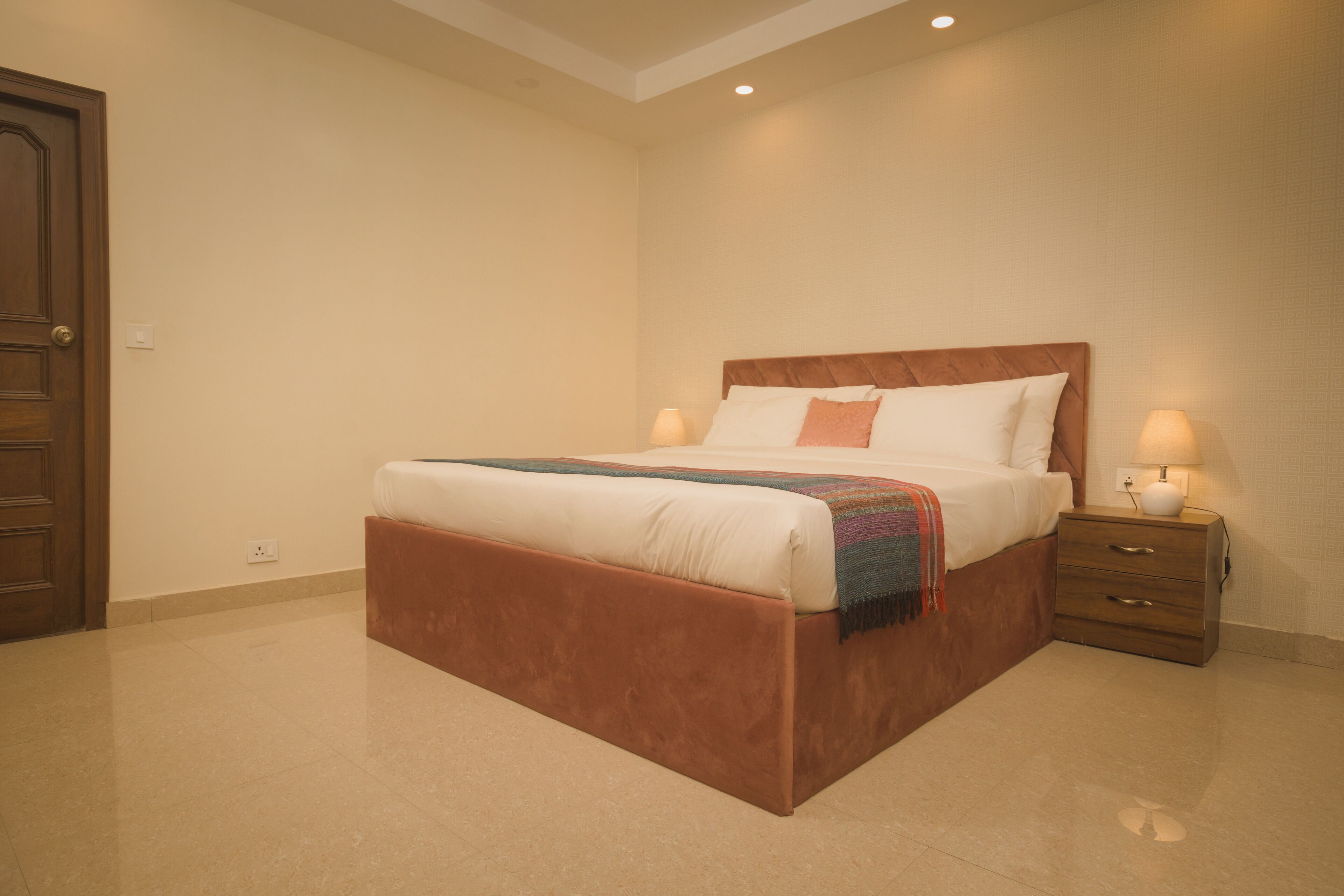 Un dormitorio con una cama grande, un cabecero de madera, dos mesitas de noche con lámparas y una puerta.