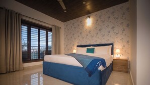 Un dormitorio con una cama grande, una mesita de noche, una ventana con cortinas y un papel tapiz floral en la pared.