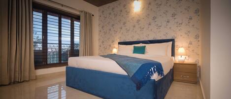 A bedroom with a large bed, a nightstand, a window with curtains, and a wall with floral wallpaper.