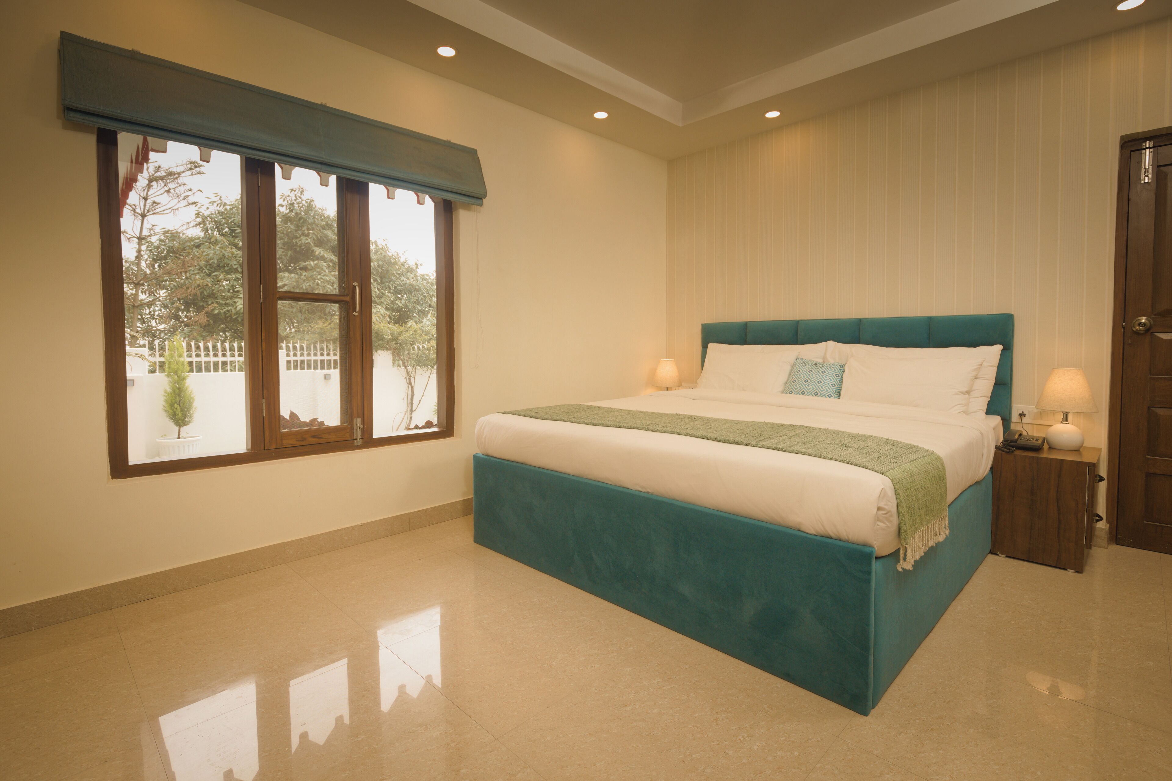 A bedroom with a large bed, a window with a view of the outside, and a door to the right.