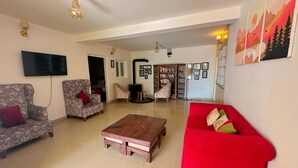 Amplia sala de estar con un sofá rojo, sillones estampados, una mesa de centro de madera y una estantería.
