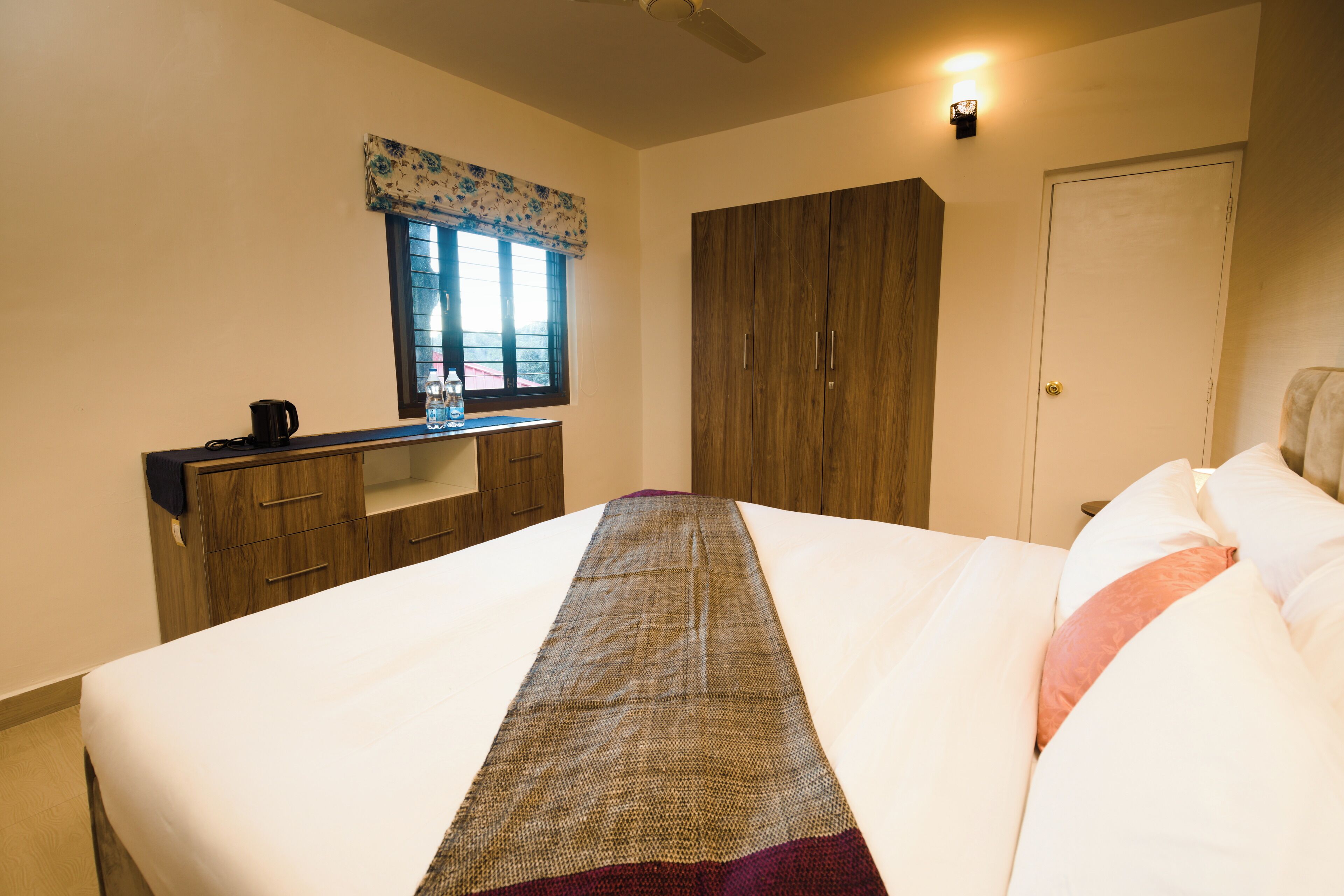 A bedroom with a bed, a desk, a wardrobe, and a window with a curtain.