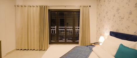 Un dormitorio con cama, cortinas, ventana con vistas y mesita de noche con lámpara.