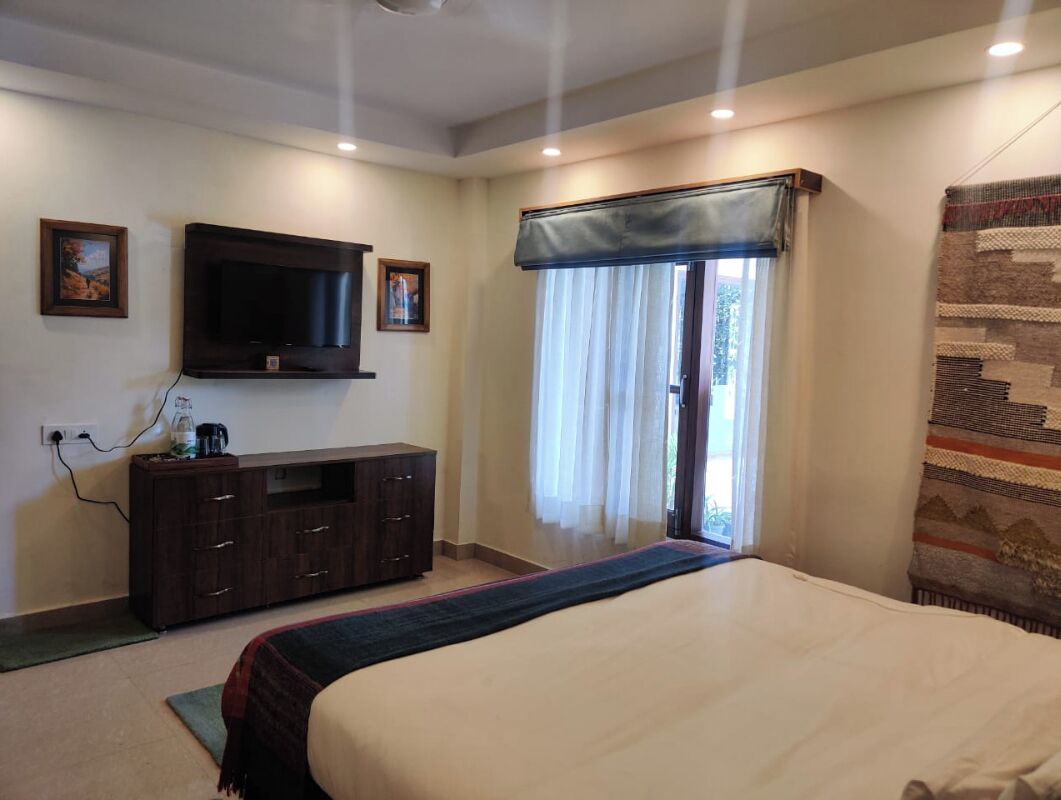 Un dormitorio con cama, televisor montado en la pared, ventana con cortinas y cómoda de madera oscura.