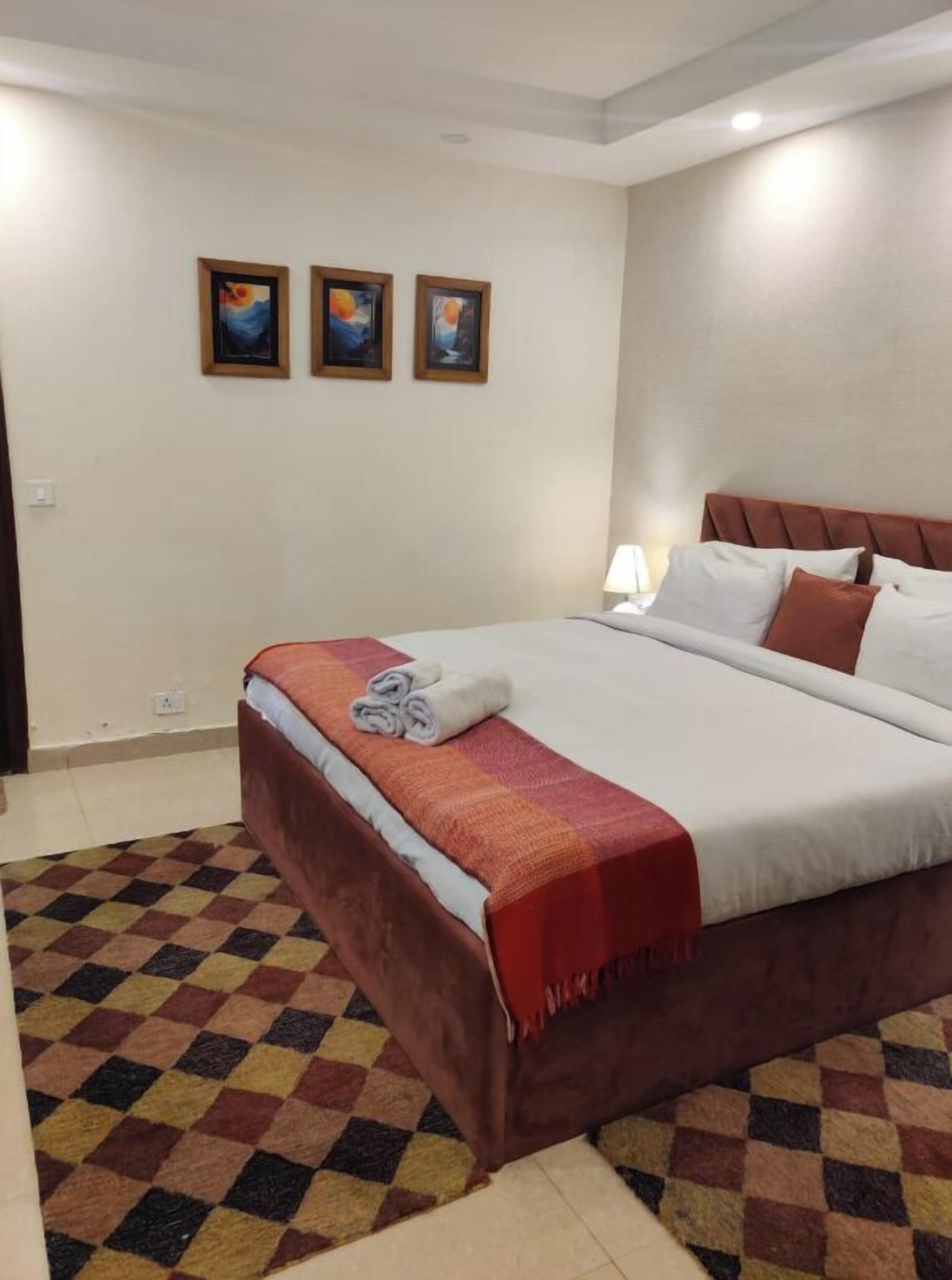 A hotel room with a large bed, a checkered floor, and three framed pictures on the wall.