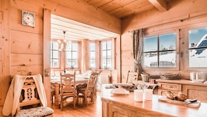 A wooden interior with a dining area, kitchen, and large windows.