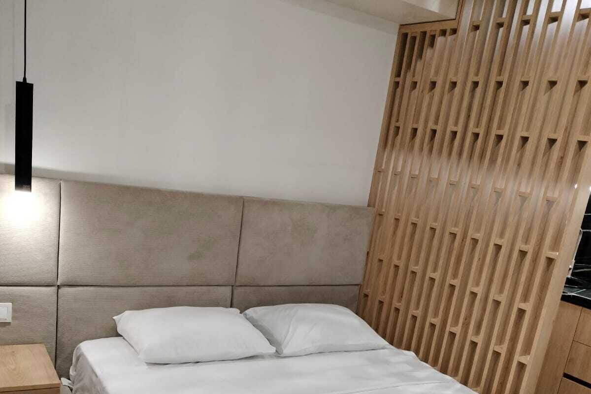 A modern bedroom with a bed, wooden headboard, bedside tables, and a hanging light fixture.
