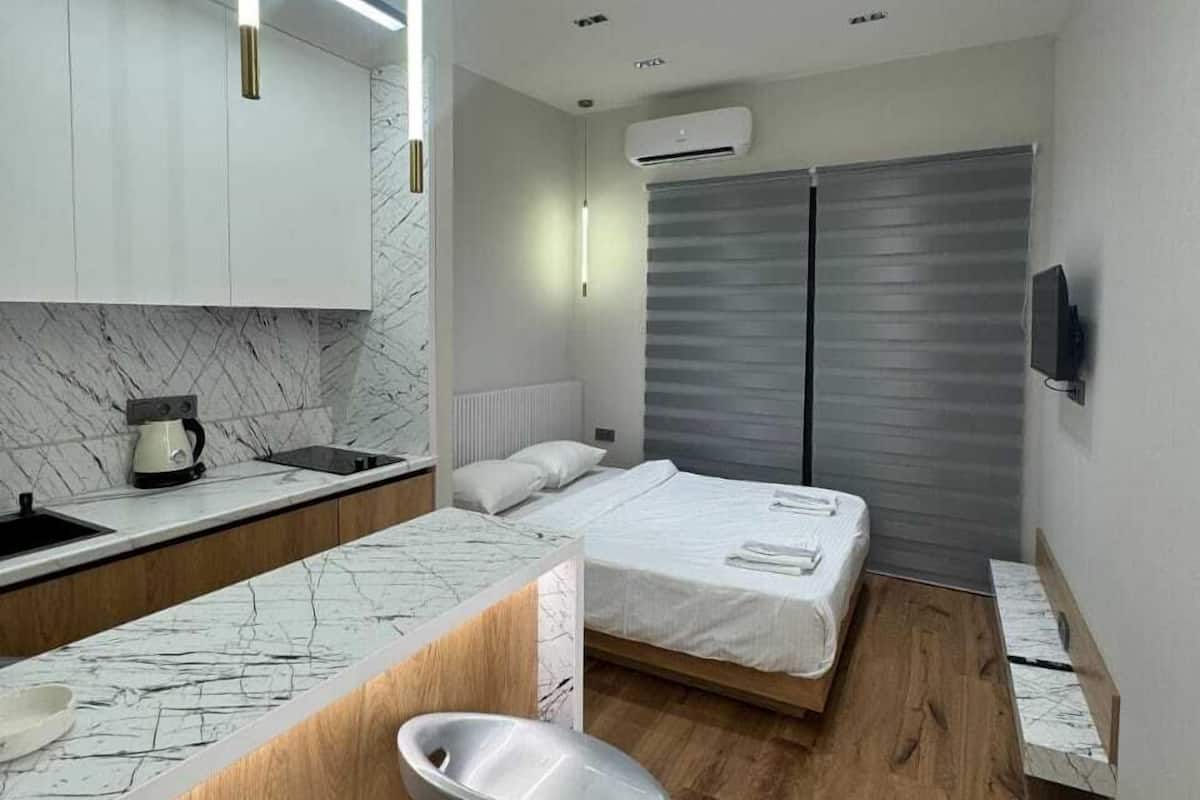 A modern, compact hotel room with a kitchen area, a bed, and a small seating area.