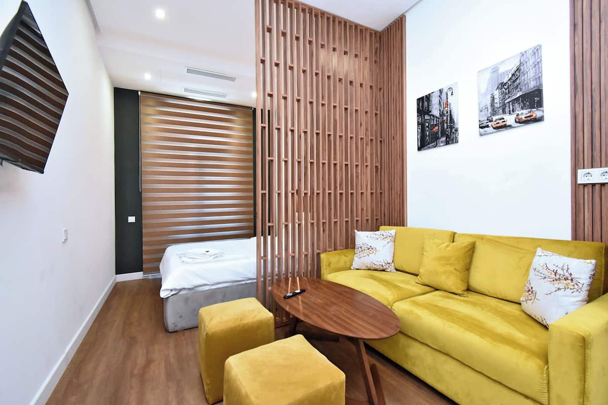 A modern room with a yellow sofa, a small wooden table, and a bed with a striped headboard.