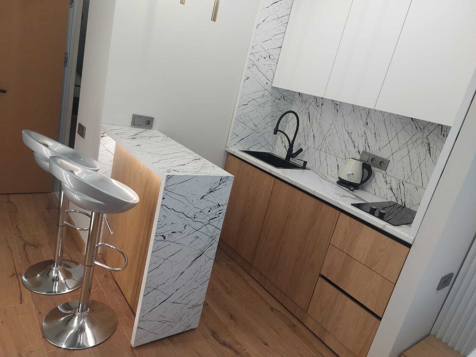 A compact kitchen with a marble backsplash, a built-in sink, and a bar stool.