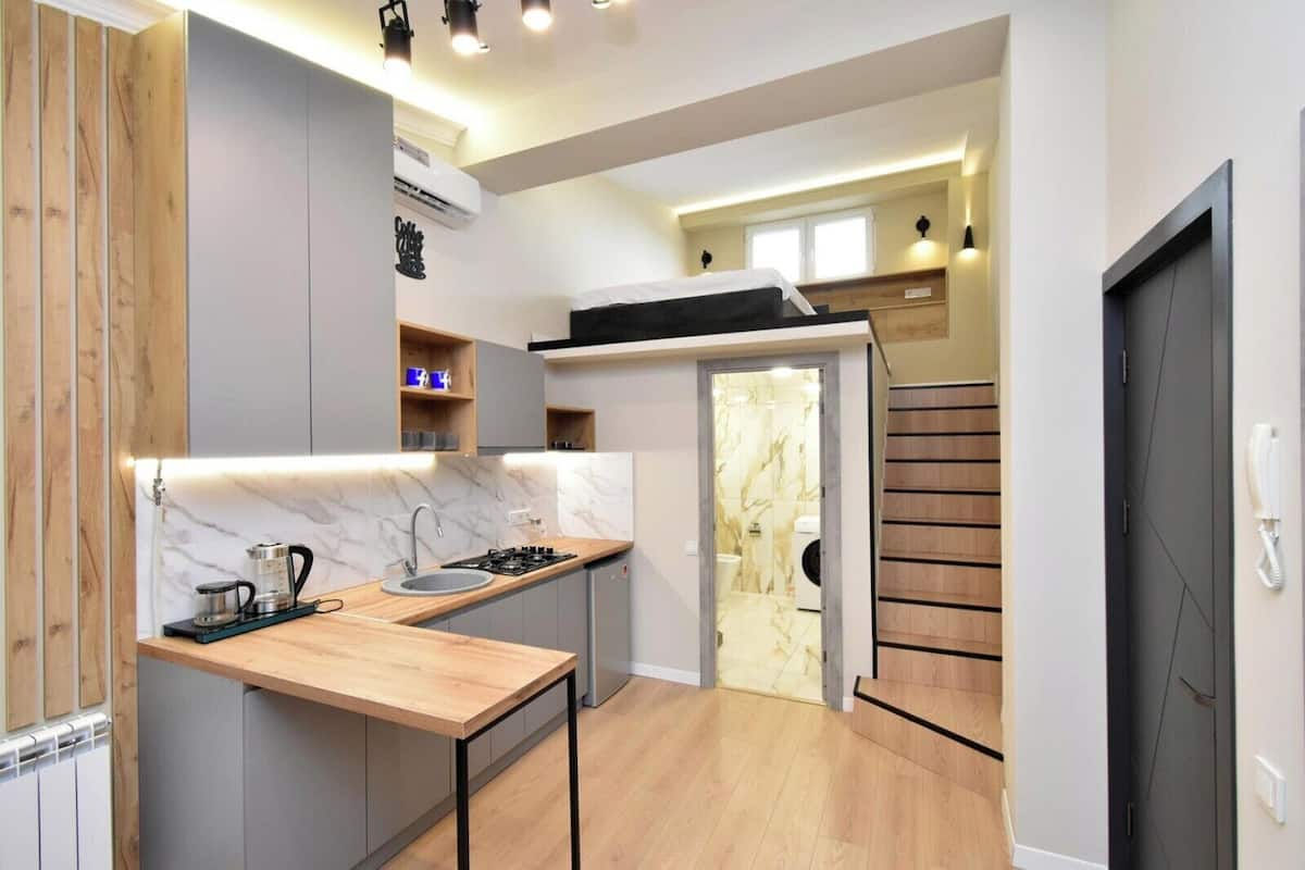 A compact kitchen with a built-in stove, sink, and wooden countertop. A staircase leads to a laundry area with a washing machine.