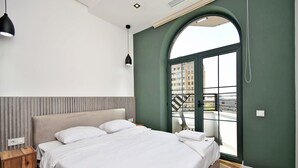 Un dormitorio moderno con una cama grande, una mesita de noche de madera, una lámpara colgante negra y vistas de la ciudad a través de un amplio ventanal de arco.