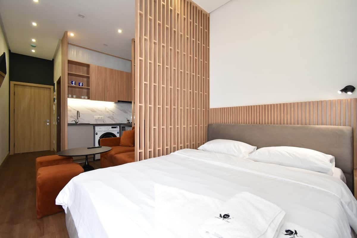 A modern hotel room with a large bed, a small kitchen area, and a seating area.