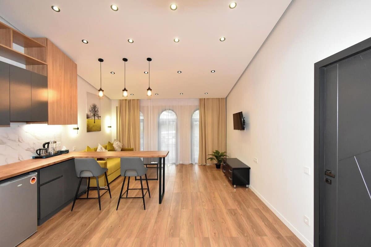A modern kitchen with wooden cabinets, a dining area with a table and chairs, and a large window with curtains.