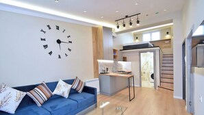 Una sala de estar moderna con un sofá azul, una mesa de centro de vidrio y un reloj de pared.