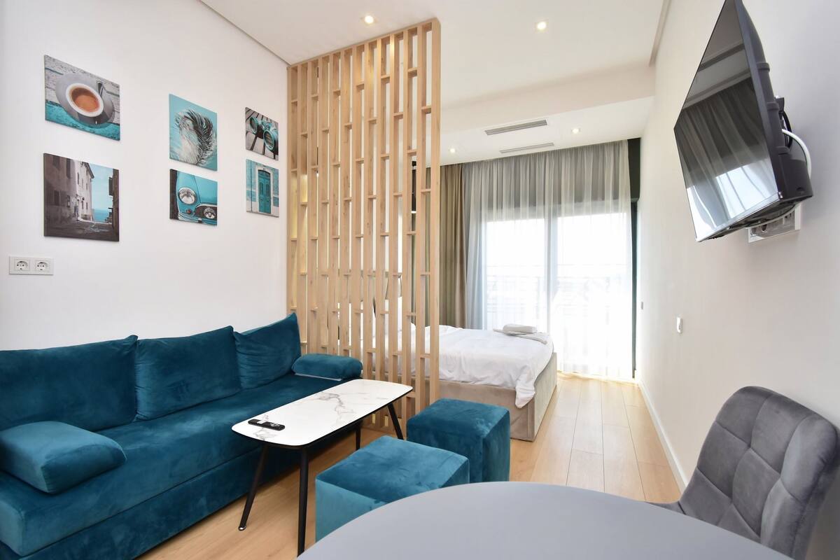 A modern hotel room with a blue sofa, a small table, a bed, and a TV mounted on the wall.