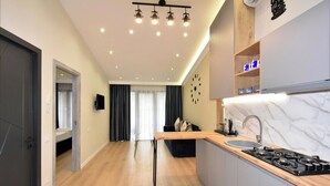 Una cocina moderna con una isla central, estufa y lavaplatos. Hay un comedor con mesa y sillas, y una sala de estar con sofá y televisor.