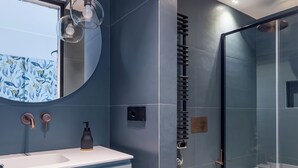 Un baño moderno con un lavabo blanco, un espejo redondo y un box de ducha de vidrio.