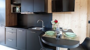 A modern kitchen with black cabinetry, a stainless steel sink, and a flat-screen TV mounted above the counter. - Ecolodge Residence Sophia (Bonifacio)
