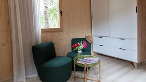 A room with a wooden wall, a green armchair, a small table with a vase of flowers, and a white wardrobe. - Ecolodge Residence Sophia (Bonifacio)