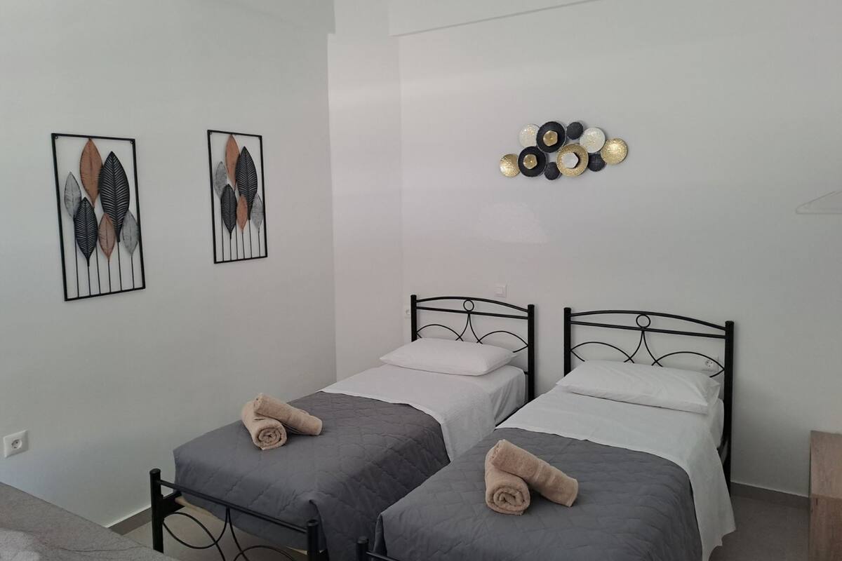 Ein Zimmer mit zwei Einzelbetten, jeweils mit einem zusammengerollten Handtuch darauf. An der Wand hängen zwei gerahmte Blätterbilder.
