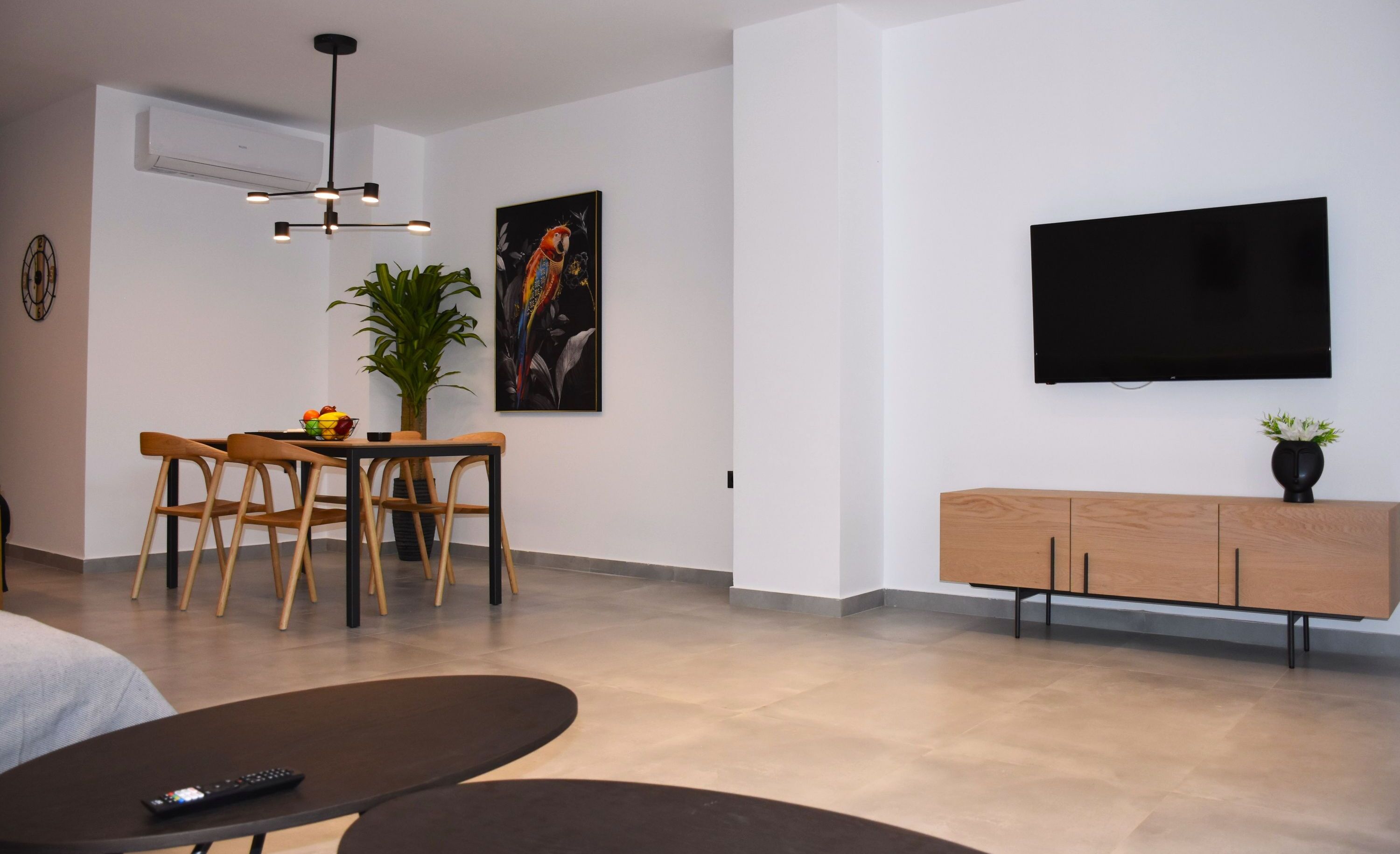 A modern living room with a dining area, a flat-screen TV mounted on the wall, and a wooden cabinet.