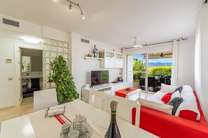 A modern living room with a TV, a dining area with a table set for tea, and a balcony with a view of the outdoors. - Villa Kalma Luxury House in Vera Playa (Vera)