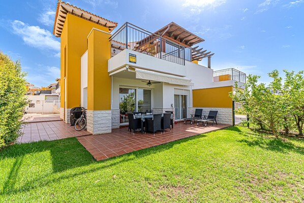 Una casa de dos pisos con un patio, muebles de exterior y una bicicleta.