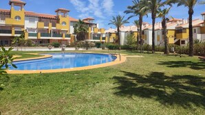 Une cour d’hôtel avec une piscine, des palmiers et un ciel d’un bleu limpide.