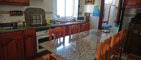 A kitchen with granite countertops, wooden cabinets, a stove, and a dining area with chairs.