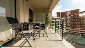 Un balcone con tavolo e sedie, una pianta in vaso e vista su un campo sportivo.