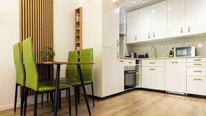 Una cucina moderna con mobili bianchi, un forno a microonde e un lavello. Sono presenti sedie verdi attorno a un tavolo di legno.