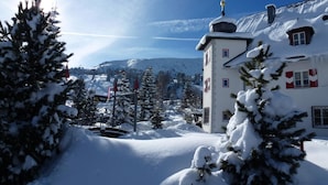 A snow-covered building with a tower, surrounded by snow-laden trees and a mountainous backdrop. - Schlosshotel Seewirt (Stadl-Predlitz)