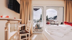 A hotel room with a bed, a desk with a chair, a television, and a view of the outdoors. - Schlosshotel Seewirt (Stadl-Predlitz)