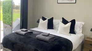 A bedroom with a large bed, a view of the outdoors, and a framed picture on the wall. - The Orchard Retreat  (Corston)