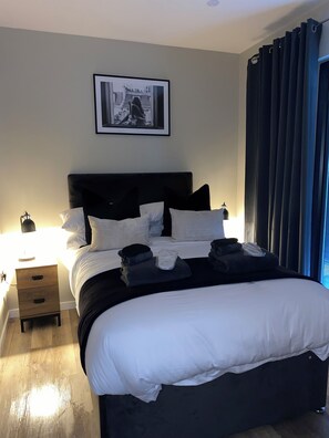 A neatly made bed with white bedding, a black headboard, and several pillows. There is a framed picture on the wall above the bed. - The Orchard Retreat  (Corston)