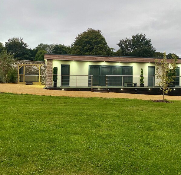 A modern building with a flat roof, large windows, and a covered outdoor area. - The Orchard Retreat  (Corston)