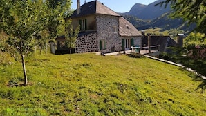 A stone house with a sloped roof, surrounded by a grassy area and trees. - Character gîte at the foot of Puy Mary in le Falgoux (Le Falgoux)