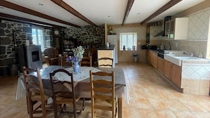A spacious dining area with a stone wall, wooden beams, and a tiled floor. - Character gîte at the foot of Puy Mary in le Falgoux (Le Falgoux)