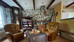 A living room with two leather chairs, a wooden coffee table, a bookshelf, and a stone wall. - Character gîte at the foot of Puy Mary in le Falgoux (Le Falgoux)