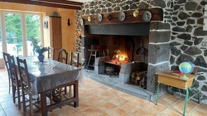 A stone fireplace with a fire, a dining table with chairs, and a small desk with a globe. - Character gîte at the foot of Puy Mary in le Falgoux (Le Falgoux)