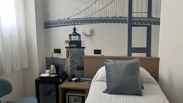 Habitación de hotel con cama, escritorio con lámpara, silla, una mesita y un mural en la pared de un puente.