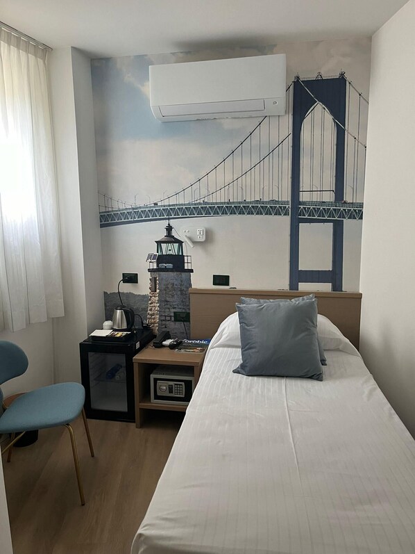 A hotel room with a bed, a desk with a lamp, a chair, a small table, and a wall mural of a bridge.