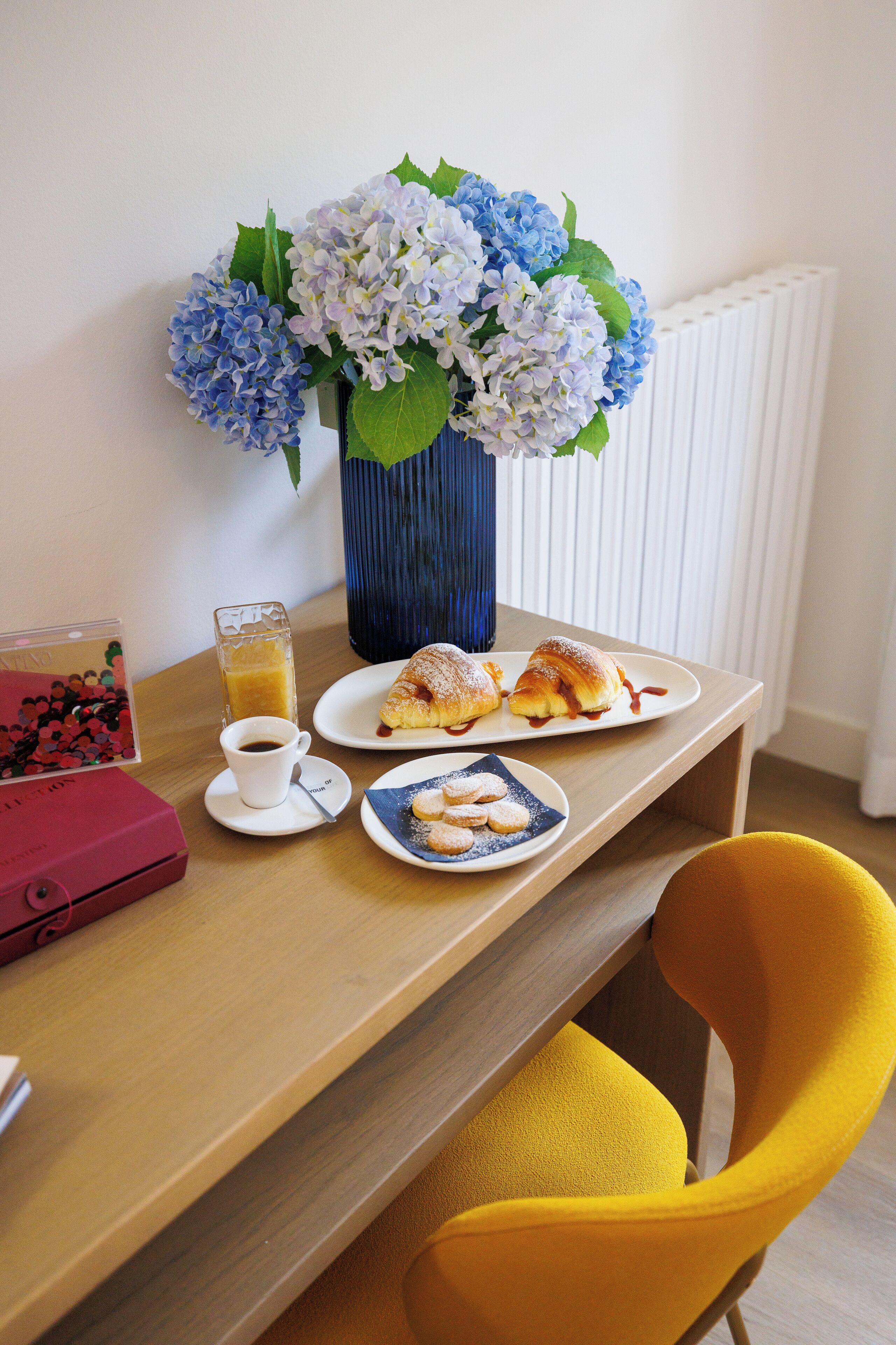 A dining table with a vase of flowers, plates of food, a cup of coffee, and a red box.
