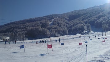 A snowy ski slope with flags marking boundaries, surrounded by forested hills.