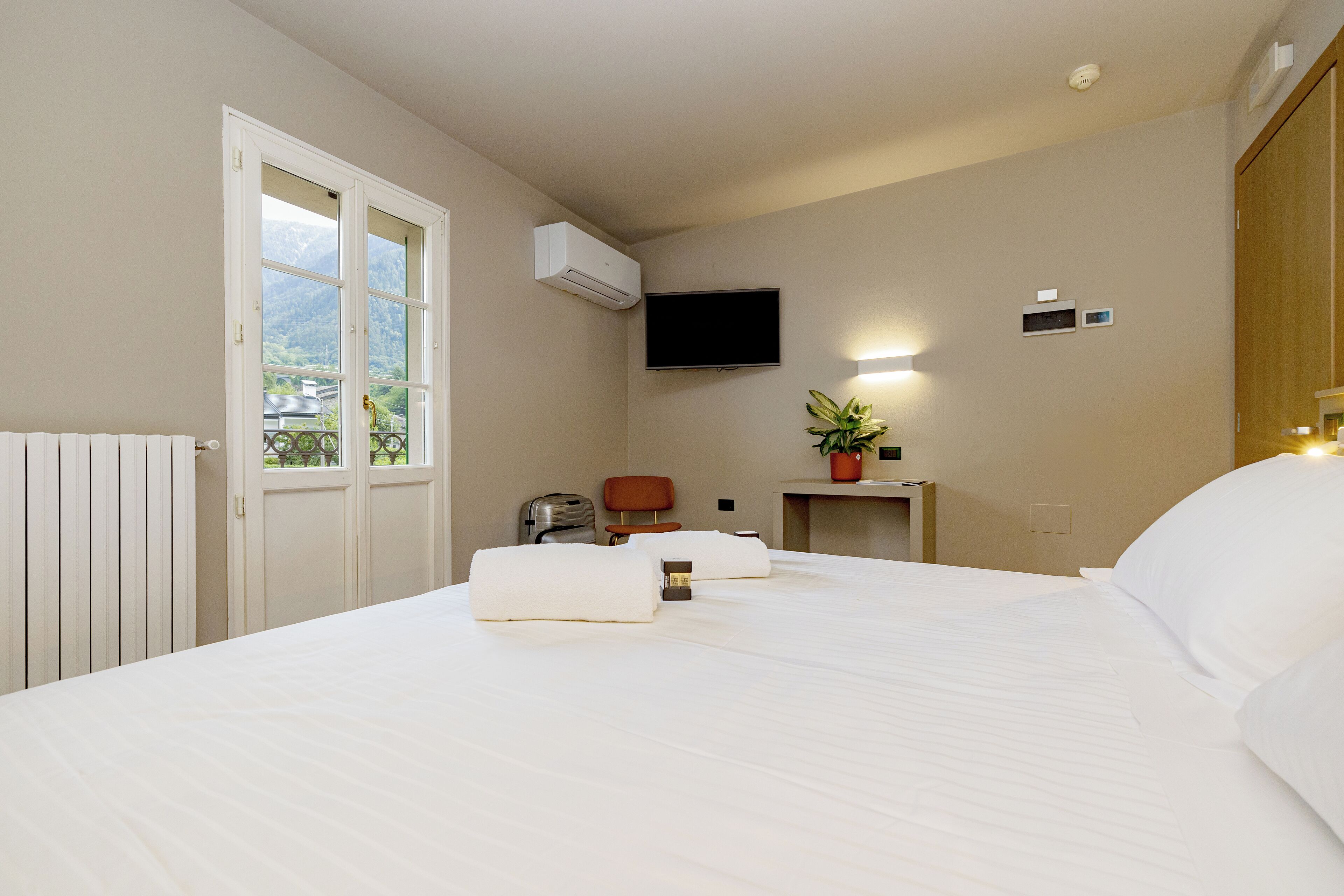 Ein Hotelzimmer mit Bett, Fernseher, Schreibtisch, Stuhl und einem Fenster mit Bergblick.