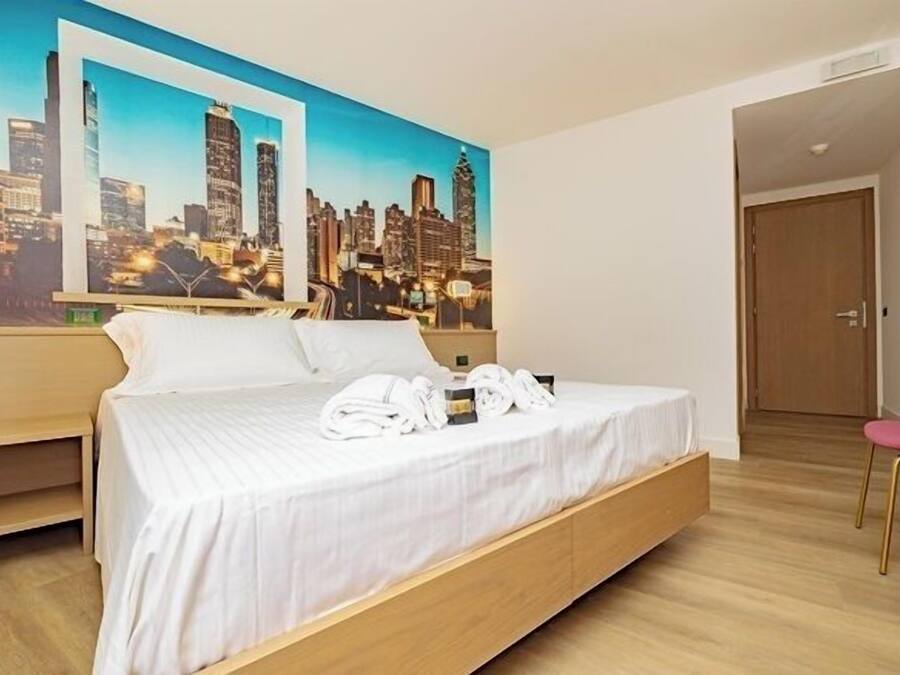 Ein Hotelzimmer mit einem Bett, einem Stadtbild-Wandbild, einem Holznachttisch und einem rosa Sessel.