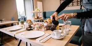 A breakfast setup with a coffee pot, cups, and a tiered dessert stand.