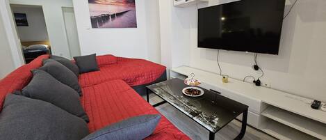 Un salon moderne avec un canapé rouge, une table basse en verre, un téléviseur à écran plat et une étagère fixée au mur.